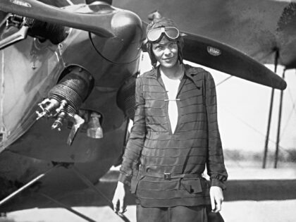 Amelia Earhart stands in front of her airplane.