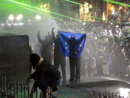 Demonstrators with an EU flag stand atop of a tomb under running water from a water cannon