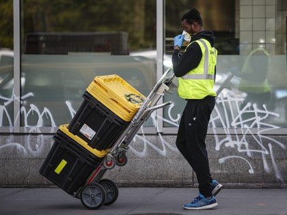 A delivery worker adjusts his mask while wearing personal protective equipment due to COVI