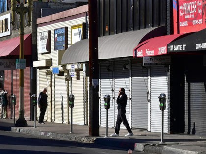 A man speaks on his cellphone in front of a row of shuttered small businesses in Los Angel