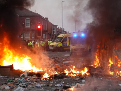 SOUTHPORT, ENGLAND - JULY 30: Riot police hold back protesters near a burning police vehic